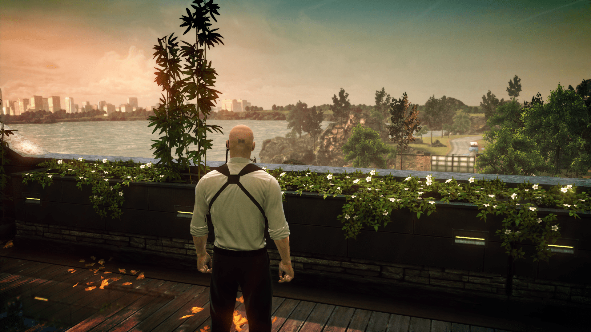 An image of Agent 47 standing on a balcony, overlooking a waterfront.  Across the water, a city can be seen in the distance.